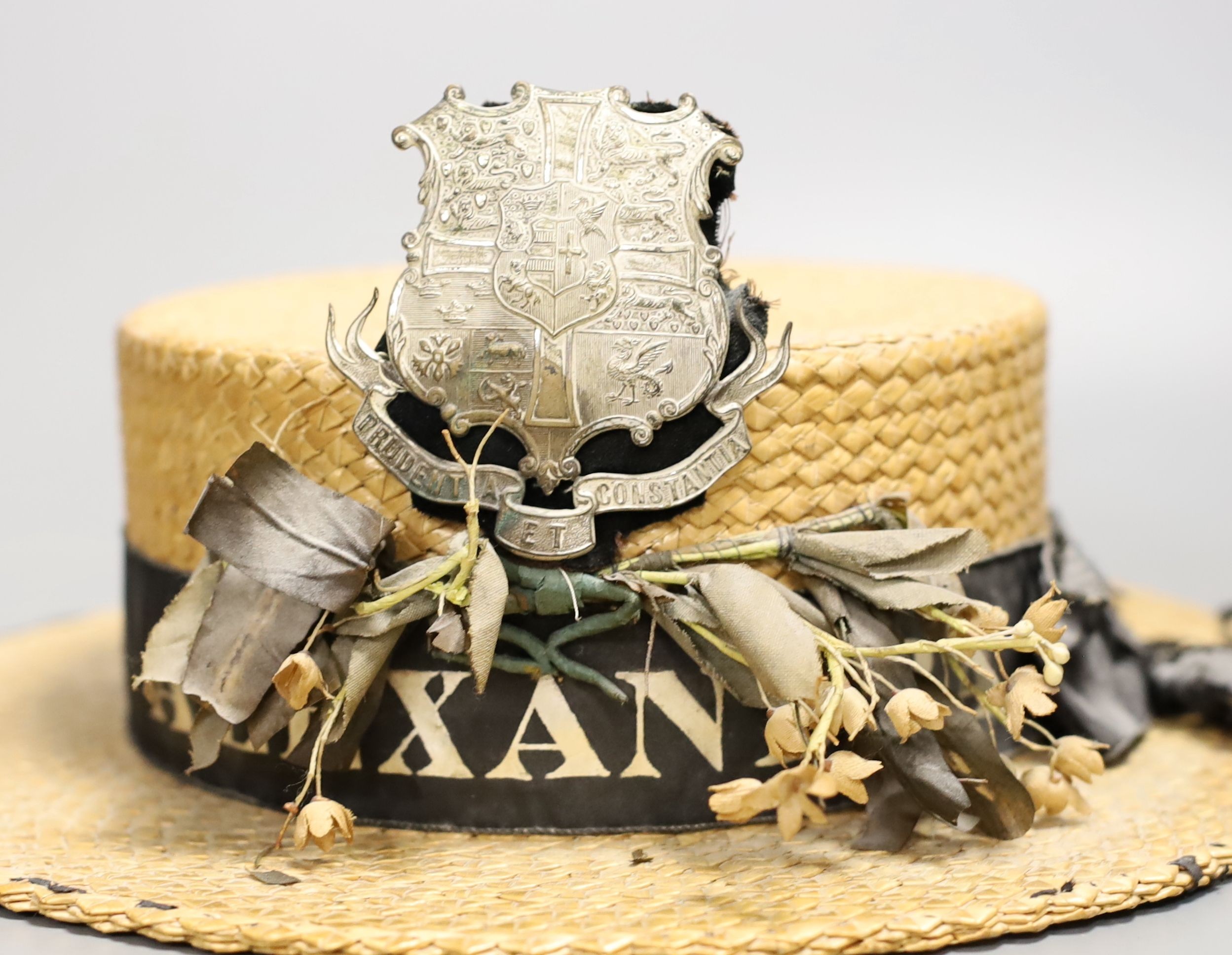 A straw boater, with crested badge and ribbon printed with ‘Alexandra’, 32 cms front to back including brim.